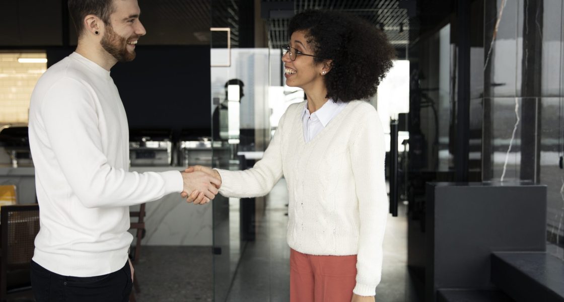 Mulher sorrindo enquanto aperta a mão de seu colega em um ambiente de trabalho moderno.